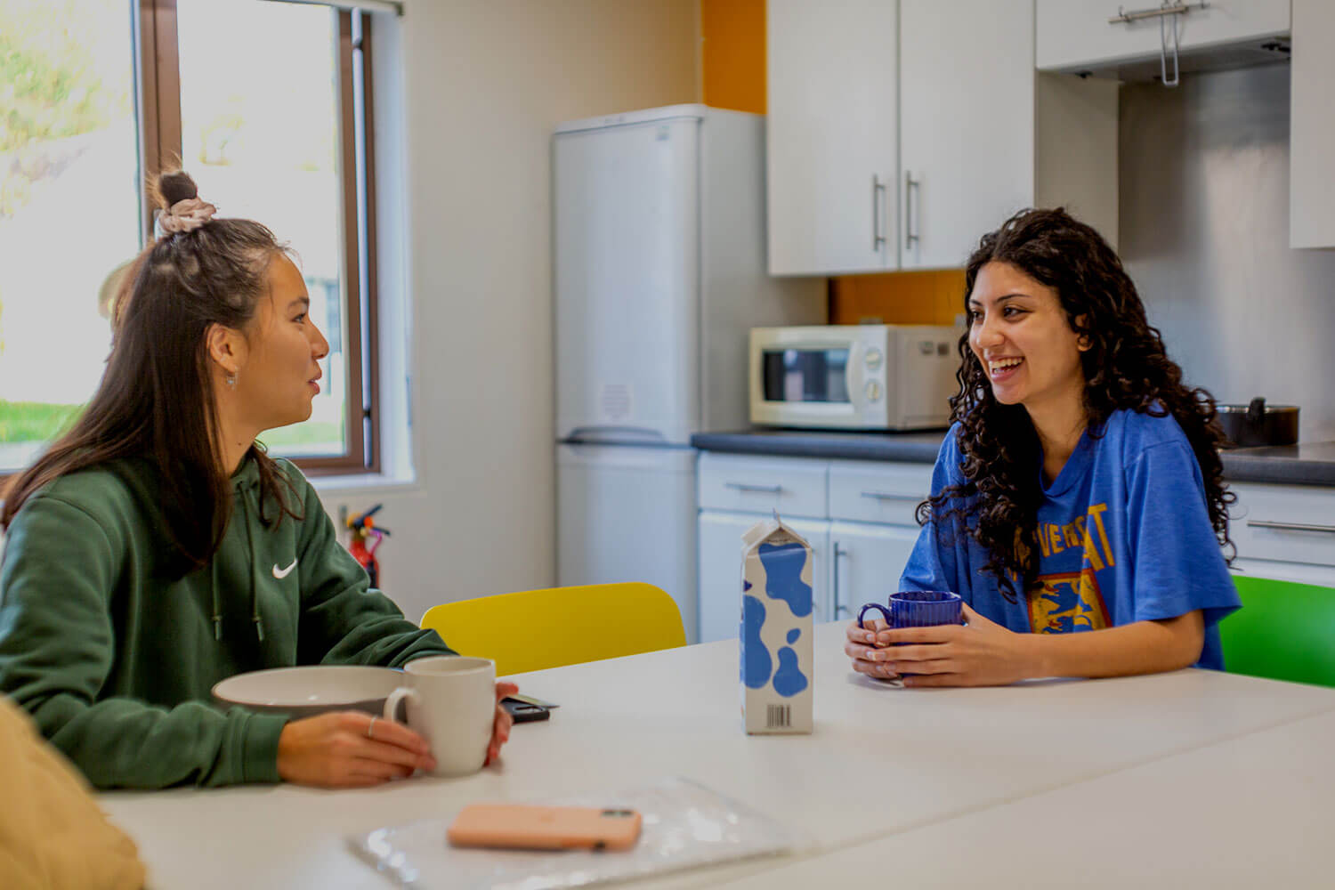 Two students in their shared kitchen, chatting over a cup of tea