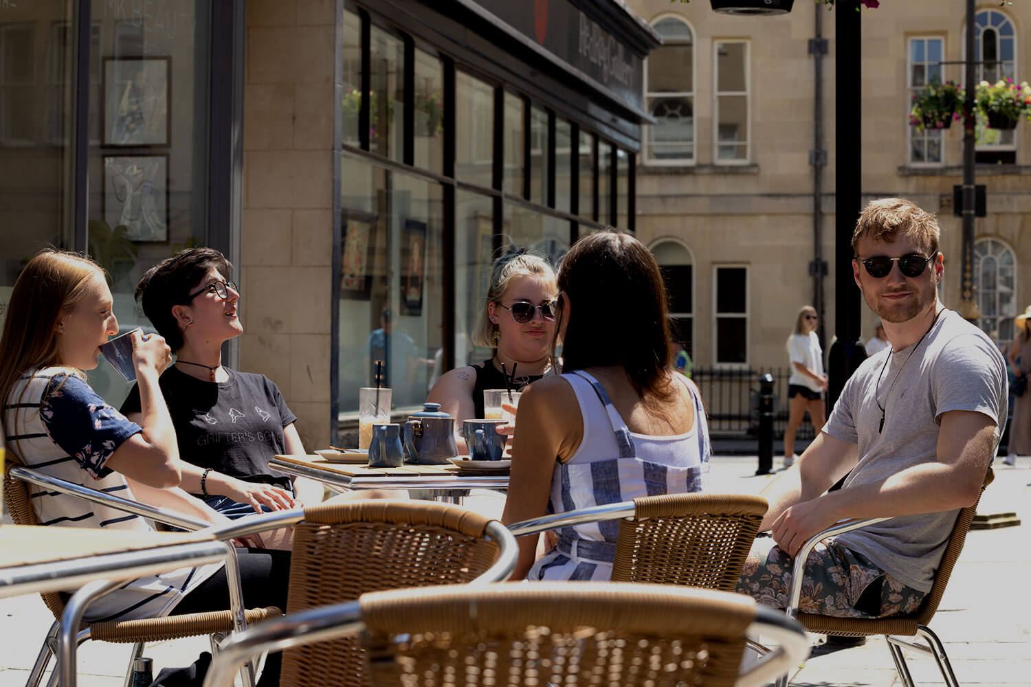 A group of students sitting outdoors at a coffee shop, with Bath's classical architecture in the background